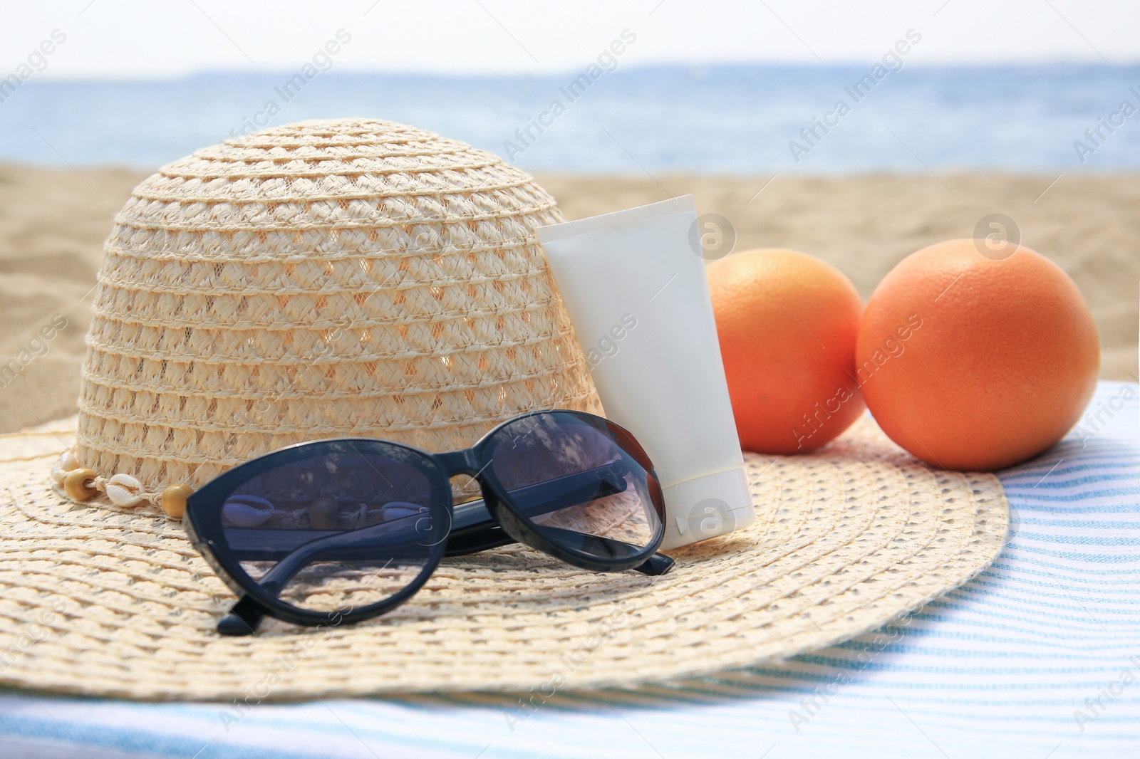 Photo of Beach accessories and oranges on sand near sea, closeup