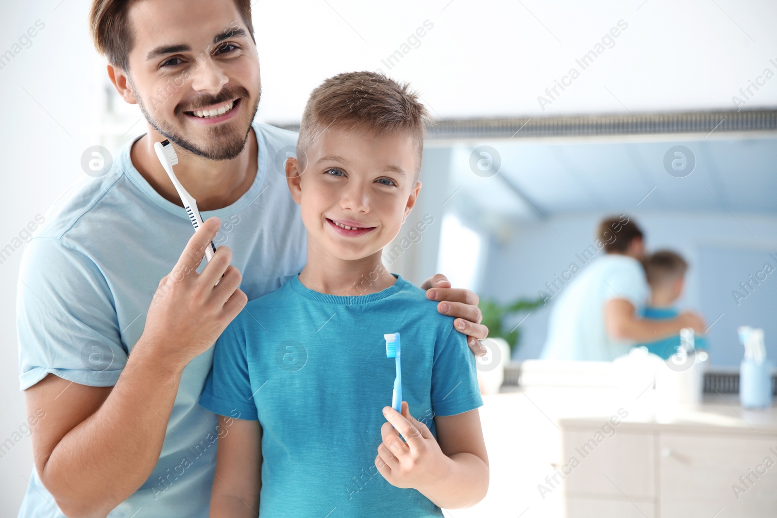 Photo of Portrait of young man and his son with toothbrushes in bathroom, space for text. Personal hygiene