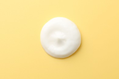 Photo of Drop of face cream on yellow background, top view