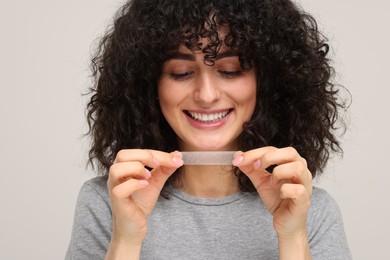 Photo of Young woman holding teeth whitening strip on light grey background