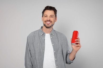 Happy man holding red tin can with beverage on light grey background