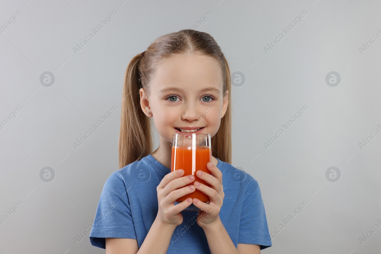 Photo of Cute little girl with glass of fresh juice on light gray background, space for text