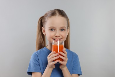 Cute little girl with glass of fresh juice on light gray background, space for text
