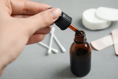 Photo of Woman dripping medical iodine into glass bottle at grey table, closeup