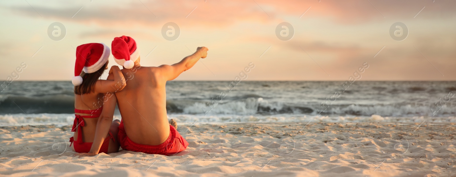 Image of Lovely couple in Santa hats together on beach, banner design. Christmas vacation