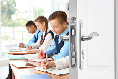 Image of Wooden door open into modern classroom with students