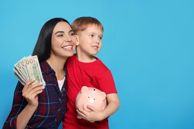 Photo of Mother holding money and her son with piggy bank on light blue background, space for text