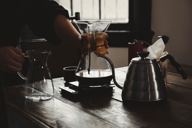 Barista with coffee maker and jug at wooden table in cafe, closeup