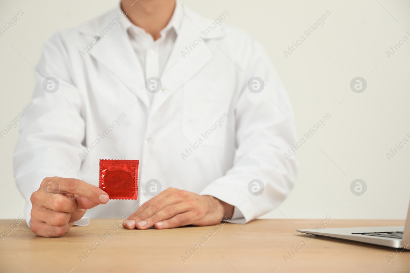 Photo of Doctor holding condom at wooden table, closeup. Safe sex concept