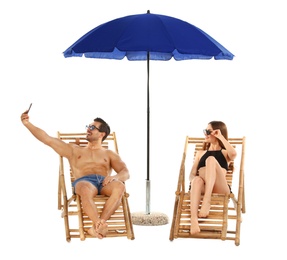 Photo of Young couple taking selfie on sun loungers under umbrella against white background. Beach accessories