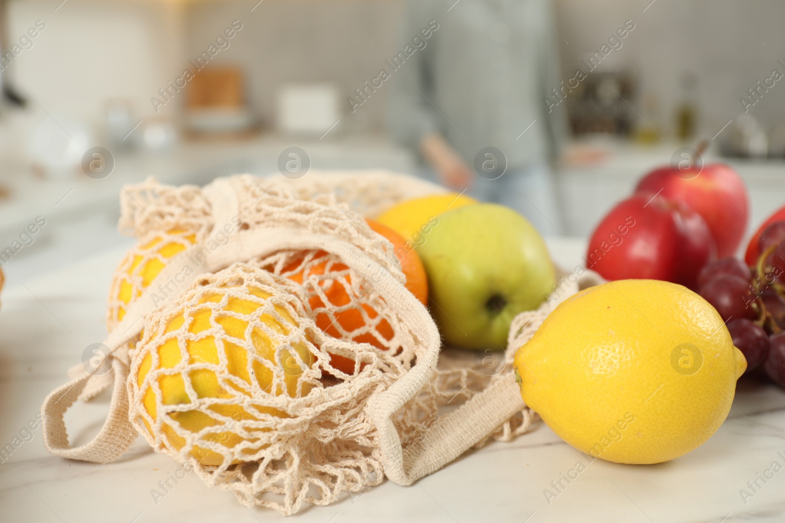 Photo of String bag of fresh fruits at light marble table, closeup