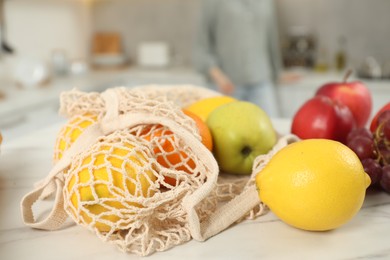 Photo of String bag of fresh fruits at light marble table, closeup