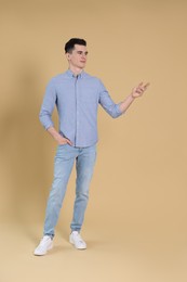 Full length portrait of handsome young man gesturing on beige background