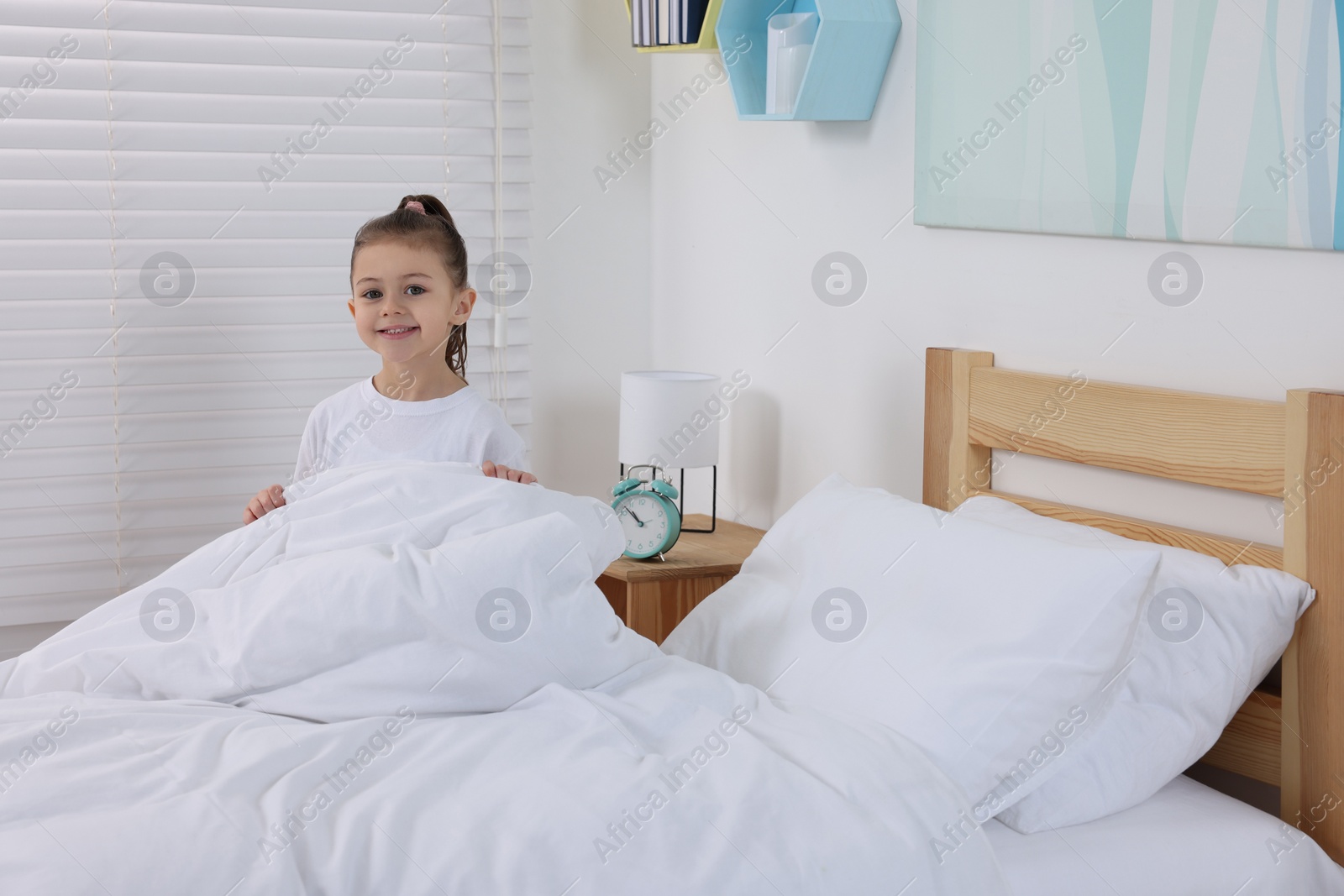 Photo of Cute girl changing bed linens in children room