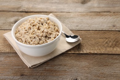 Photo of Tasty boiled oatmeal in bowl and spoon on wooden table, space for text