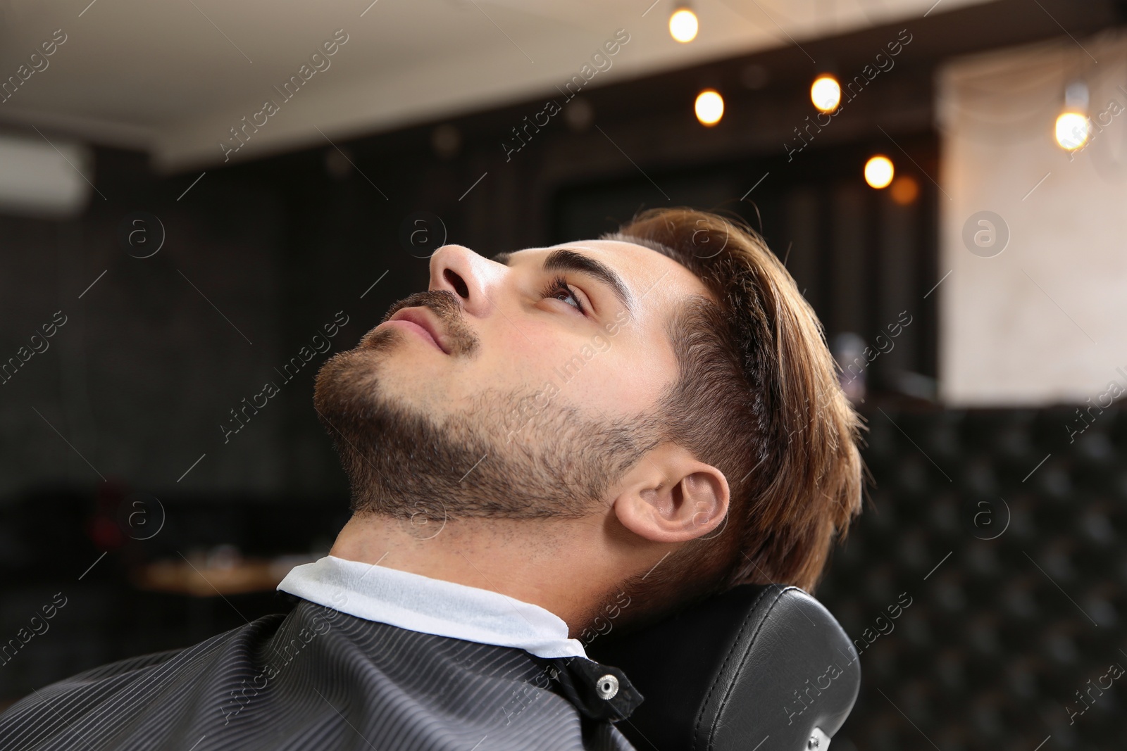 Photo of Young man visiting barbershop. Professional shaving service