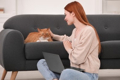 Photo of Woman stroking cat while working with laptop at home