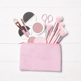 Cosmetic bag with makeup products and beauty accessories on white wooden background