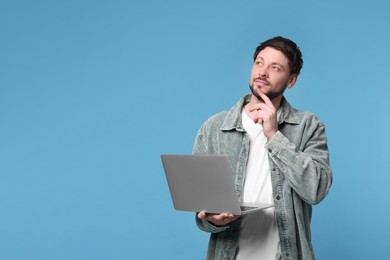 Handsome man with laptop on light blue background, space for text