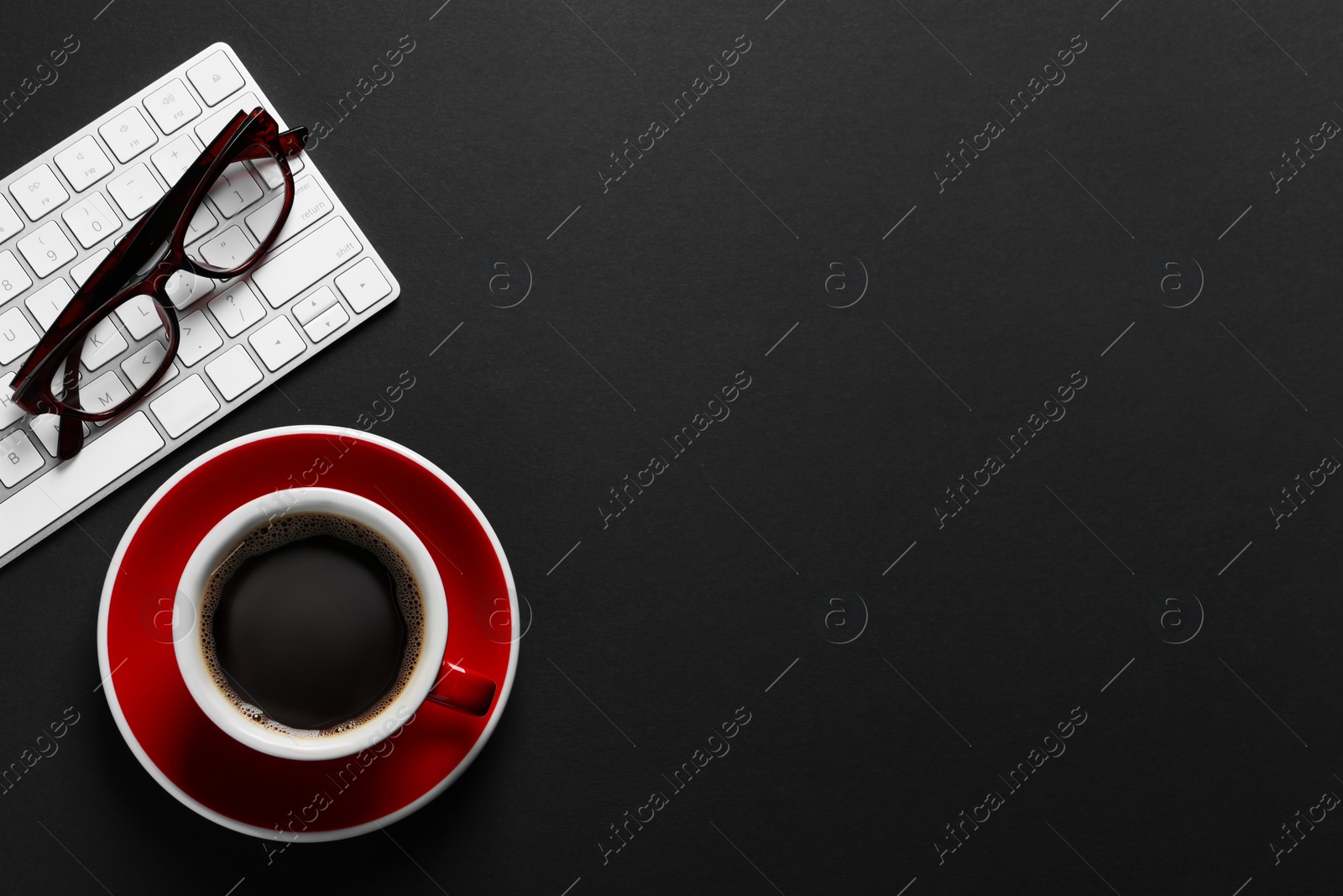 Photo of Cup with aromatic coffee, glasses and keyboard on black background, flat lay. Space for text