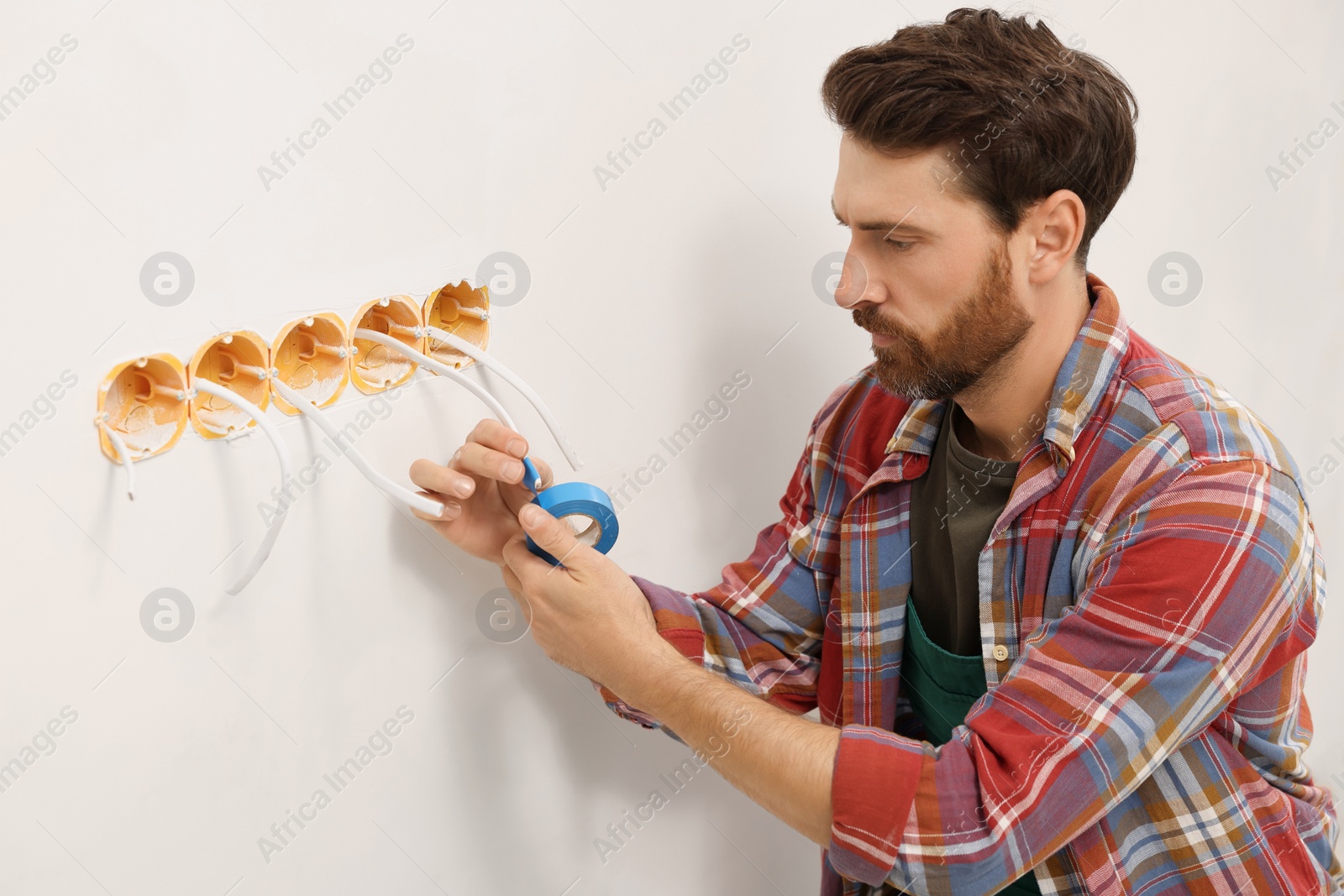 Photo of Electrician fixing wires with insulating tape indoors