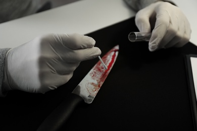 Photo of Detective taking DNA sample of blood from knife at table, closeup