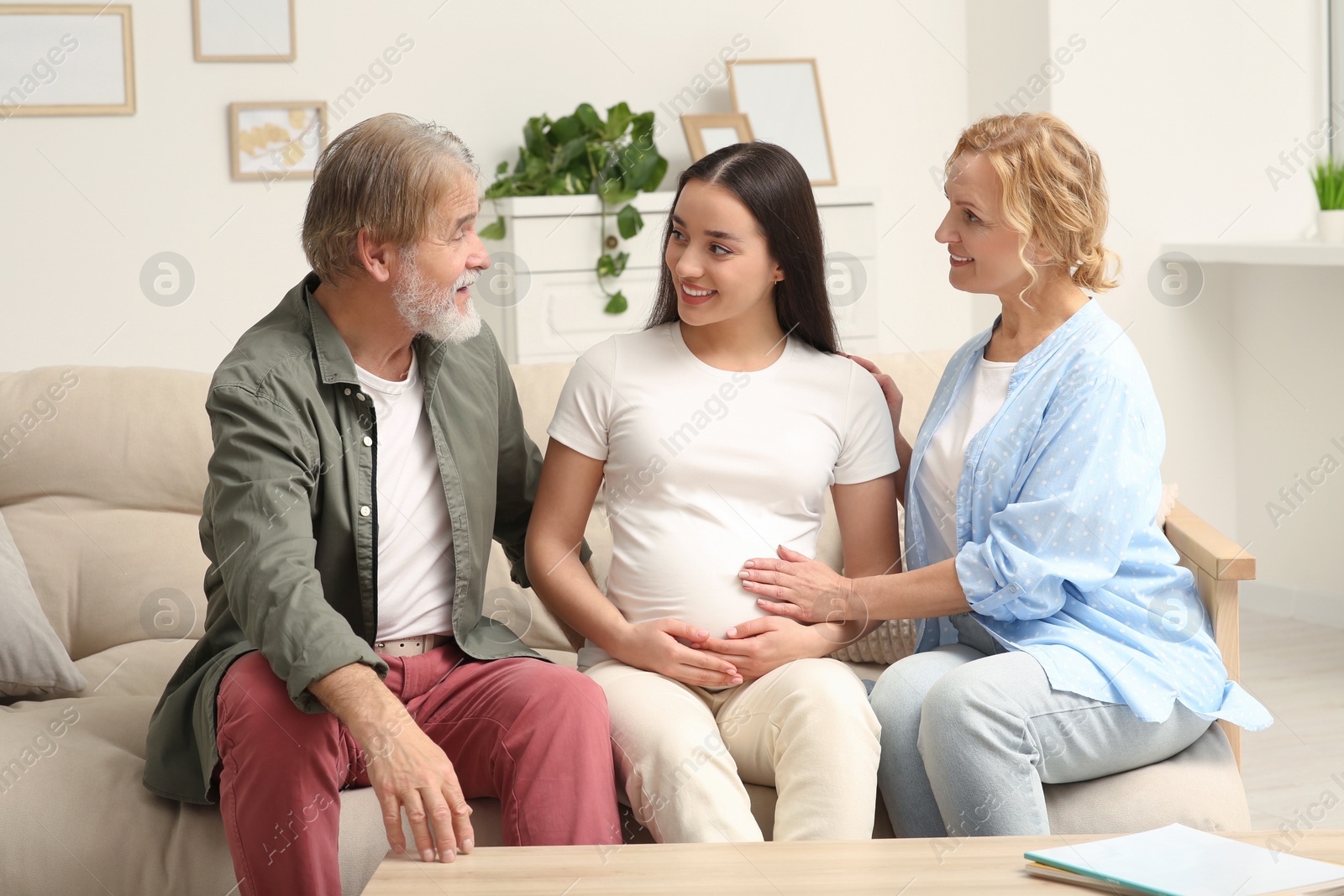 Photo of Happy pregnant woman spending time with her parents at home. Grandparents' reaction to future grandson