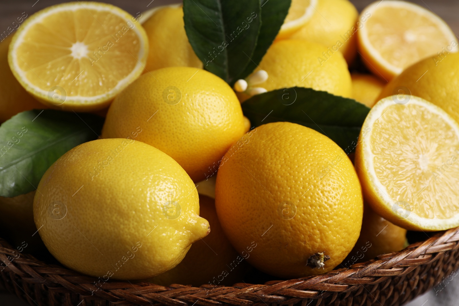 Photo of Many fresh ripe lemons in wicker bowl, closeup