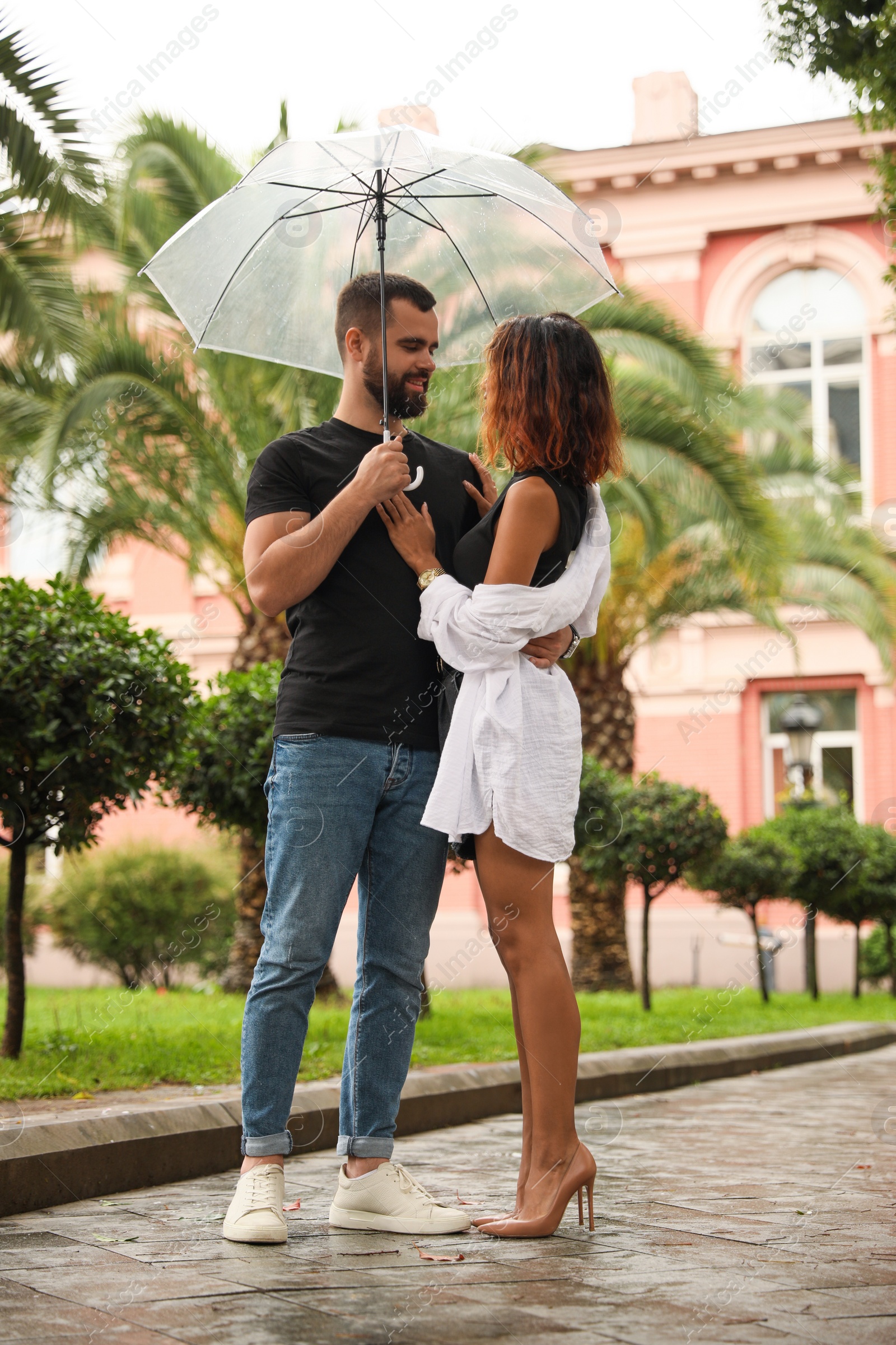 Photo of Young couple with umbrella enjoying time together under rain on city street