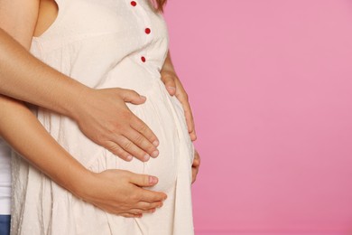Photo of Man hugging his pregnant wife on pink background, closeup. Space for text