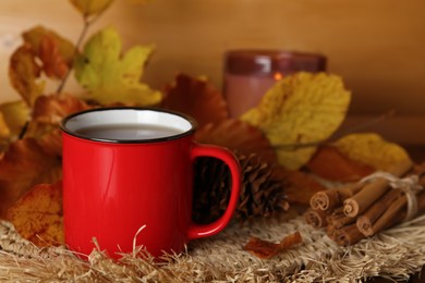 Photo of Cup of hot drink, pine cone, cinnamon sticks and autumn leaves on wicker mat. Space for text