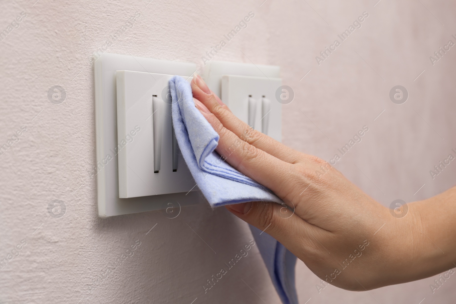Photo of Woman cleaning light switch with rag indoors, closeup