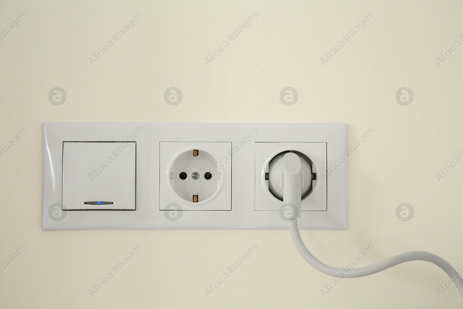 Photo of Power sockets with inserted plug and light switch on white wall indoors