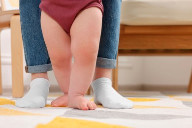Photo of Mother supporting her baby son while he learning to walk on carpet at home, closeup. Space for text