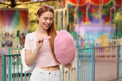 Beautiful woman eating cotton candy at funfair. Space for text