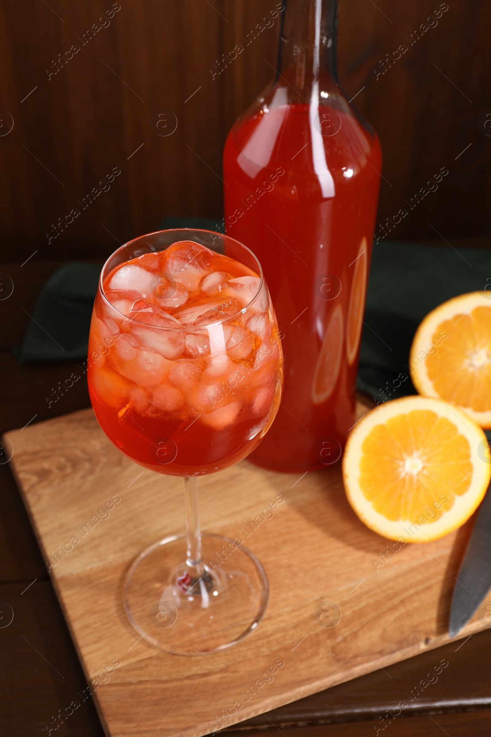 Photo of Aperol spritz cocktail and ice cubes in glass and bottle on wooden table