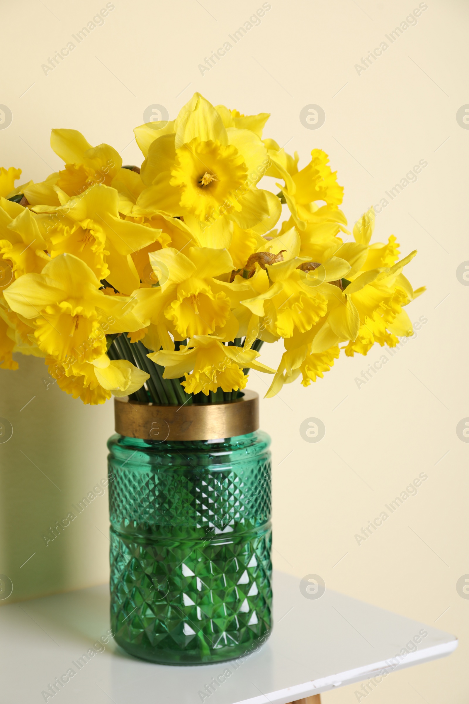 Photo of Beautiful daffodils in vase on white table near light wall