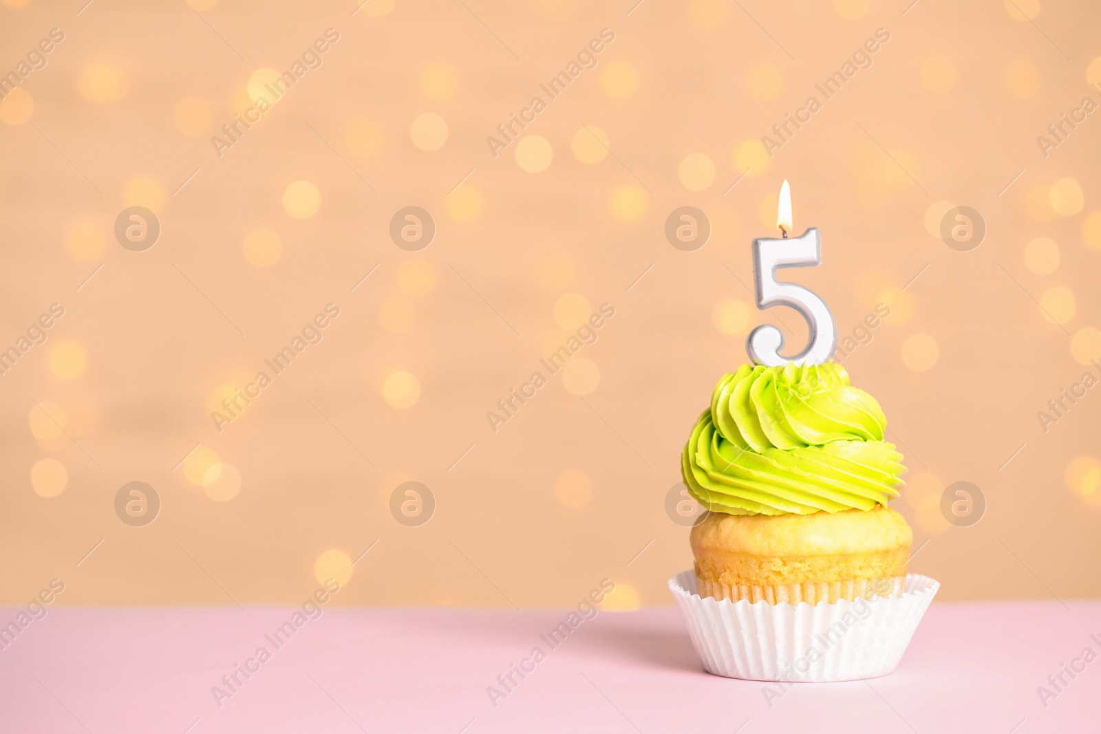 Photo of Birthday cupcake with number five candle on table against festive lights, space for text