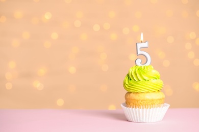 Photo of Birthday cupcake with number five candle on table against festive lights, space for text