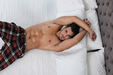 Photo of Sexy young man lying on bed with soft pillows at home, top view