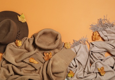 Photo of Flat lay composition with sweater and dry leaves on orange background, space for text. Autumn season