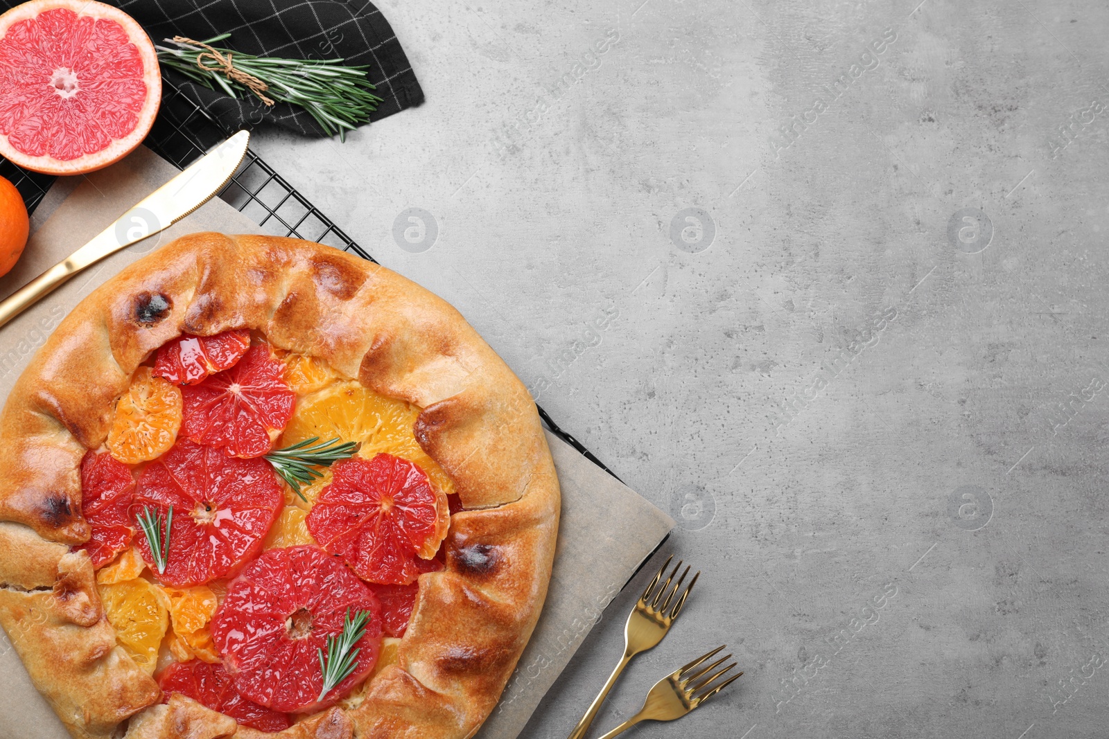 Photo of Tasty galette with citrus fruits and rosemary served on grey table, flat lay. Space for text