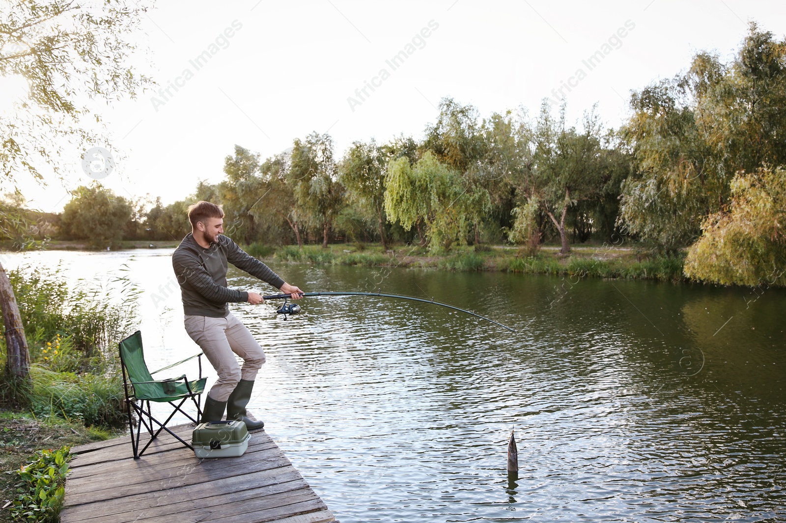 Photo of Man with rod fishing on wooden pier at riverside. Recreational activity