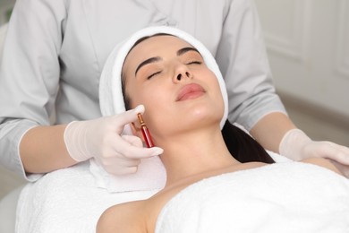 Professional cosmetologist holding skincare ampoule while working with client in clinic, closeup