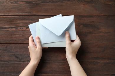 Photo of Woman with paper envelopes at wooden table, top view