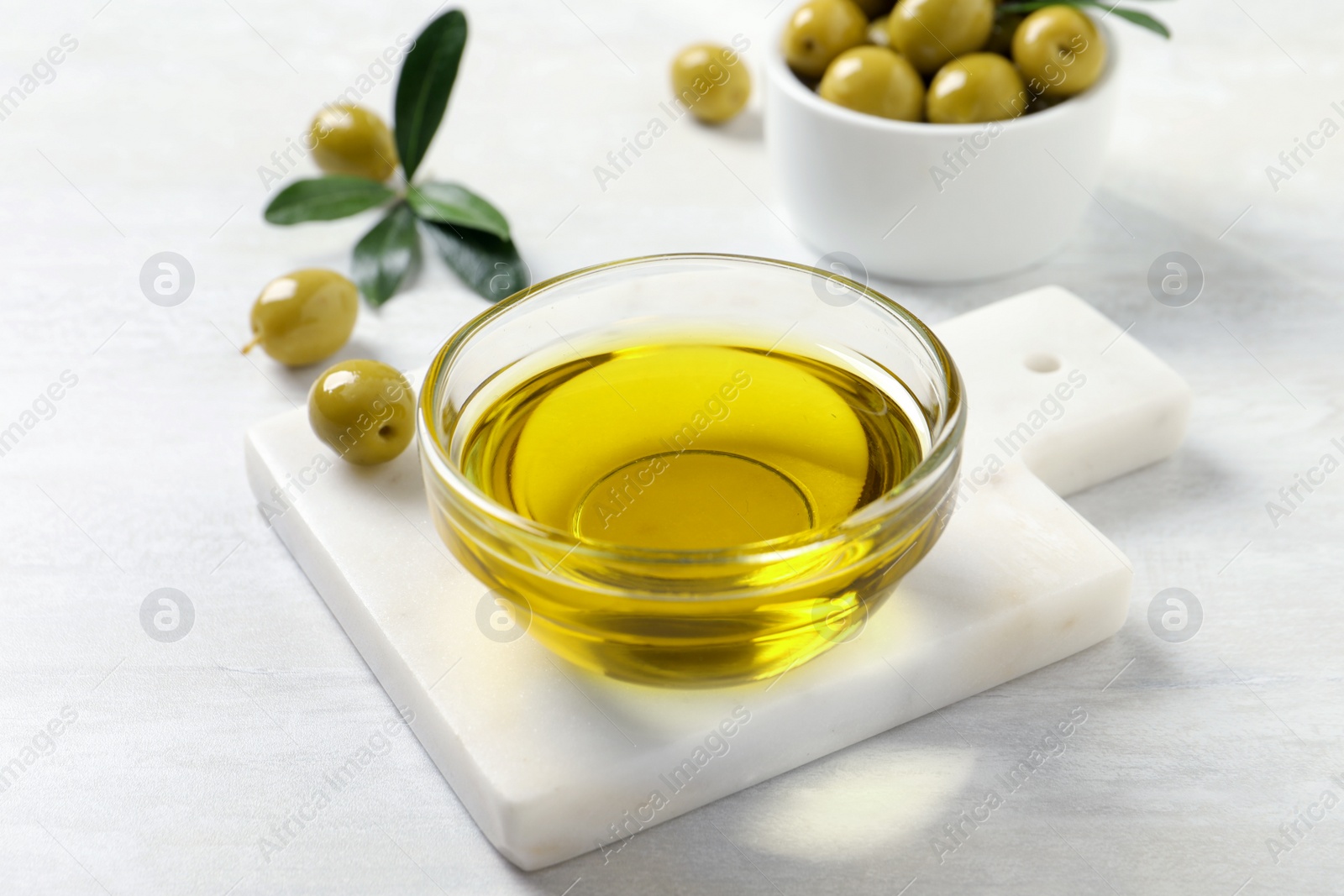 Photo of Glass bowl with fresh olive oil on white wooden table