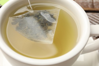 Photo of Tea bag in cup with hot drink on table, closeup