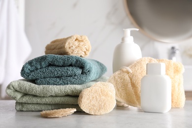 Photo of Natural loofah sponges, towels and cosmetic products on table in bathroom