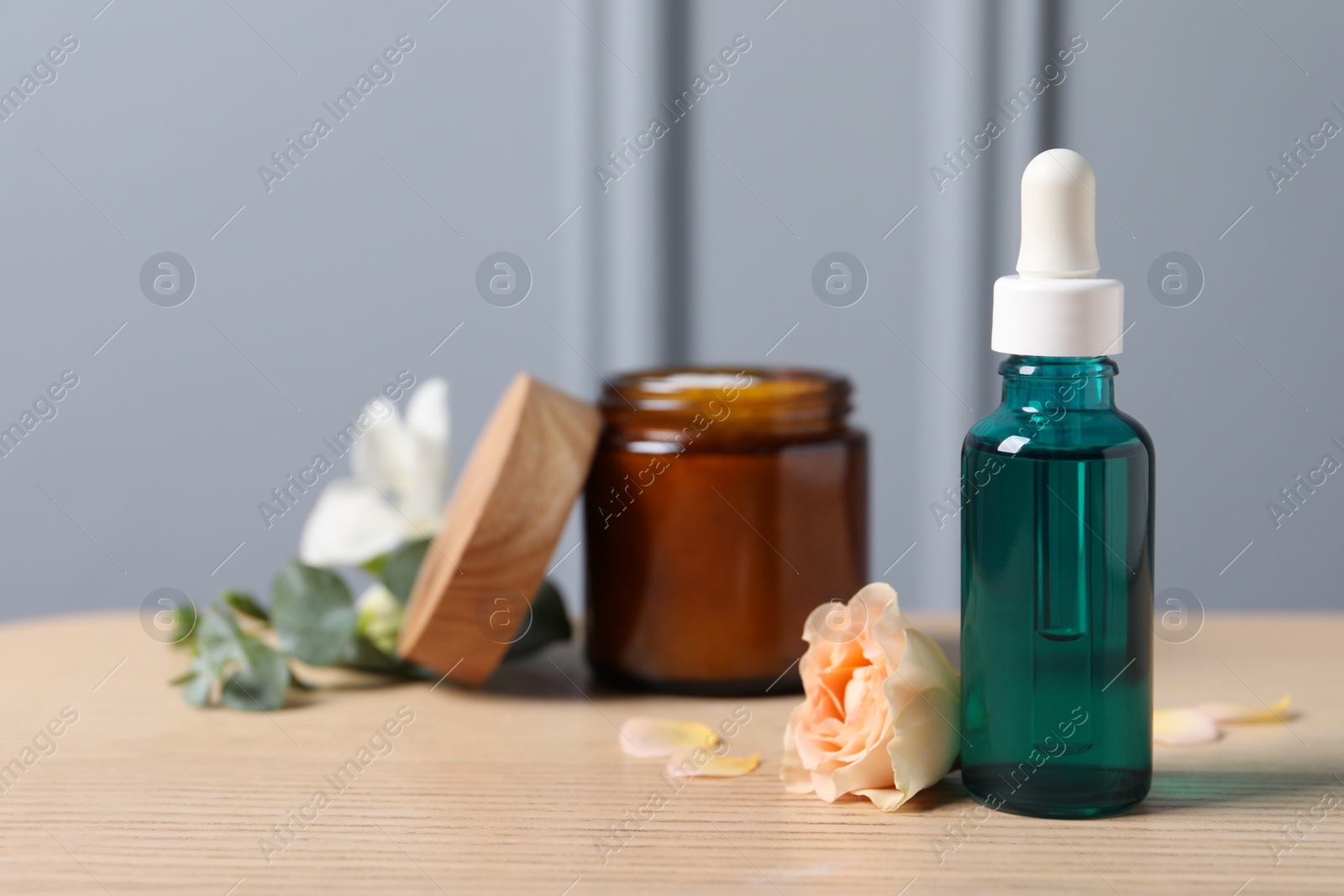 Photo of Bottle of cosmetic serum, cream jar and beautiful flower on wooden table