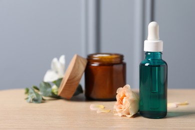 Bottle of cosmetic serum, cream jar and beautiful flower on wooden table